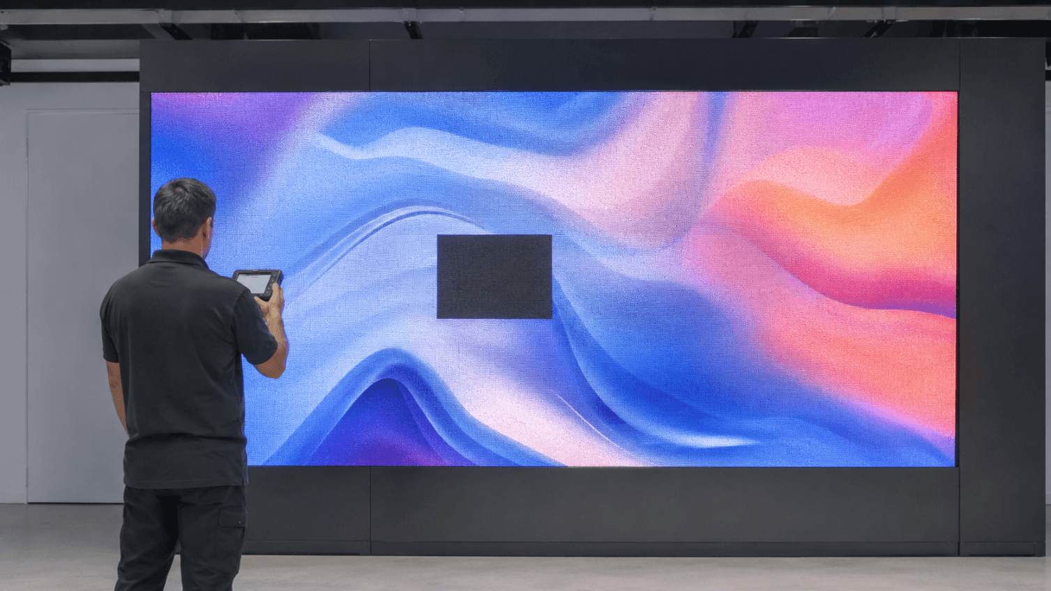 Técnico inspeciona um módulo apagado no centro de um painel de LED indoor.